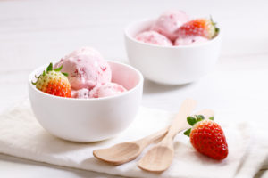 strawberry ice cream scoops in white bowl with fresh strawberries